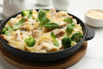 Delicious pasta Alfredo with chicken, cheese, creamy sauce, broccoli and basil on white table, closeup