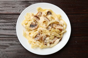 Tasty Alfredo pasta with chicken and mushrooms on wooden table, top view
