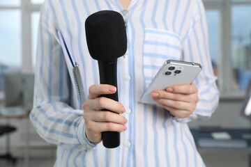 Journalist with microphone and smartphone indoors, closeup
