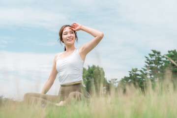 Obraz premium 草原の中でヨガ・ストレッチ・ピラティス・ボディケアをする女性(ヘルスケア・ダイエット・健康維持) 