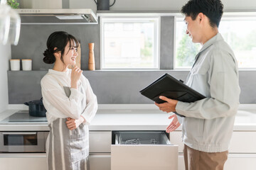 キッチンで水道屋・設備屋に食洗機・食器洗浄器の説明を受ける主婦の女性
