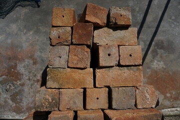 Stack of rustic, weathered bricks with natural textures and earthy tones, set against a rough concrete wall background, perfect for construction or industrial themed visuals.