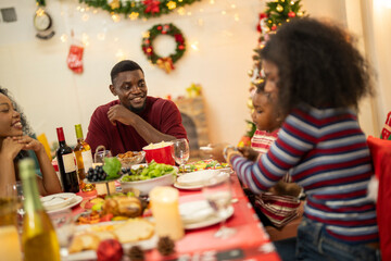 A warm Christmas family dinner with a father serving food to his young child, surrounded by festive decorations, a Christmas tree, and a holiday table spread. Joyful and cozy holiday atmosphere.