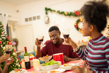A joyful family shares a Christmas meal together, passing food and creating holiday memories. Decorated tree, festive lights, and presents in the background add warmth to cozy celebration atmosphere.
