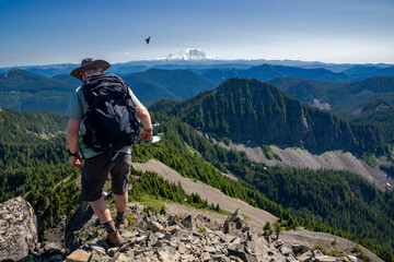 Athletic adventurous male hiker, hiking down a ridge on top of a mountain with Mount Rainier in the background during a beautiful sunny day. 