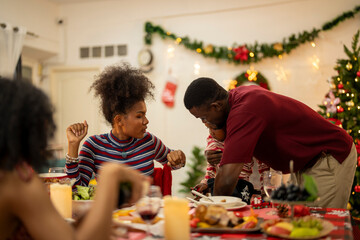 A festive family Christmas dinner setting with a decorated tree in the background. The family gathers around a beautifully decorated table, sharing food, joy, and warmth in the holiday spirit.