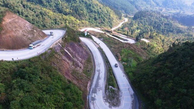 This drone footage captures the stunning curves of the Ha Giang Loop in North Vietnam, showcasing winding mountain roads surrounded by lush greenery. Vehicles navigating the sharp turns.