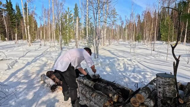 Survival in the wild. Man in black fur coat and snowshoes in winter forest
