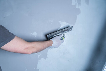 A worker uses a trowel to apply microcement adhesive to repair a wall in a residential area.