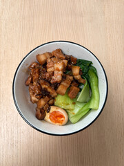 A bowl of rice with pork belly, egg, and bok choy.