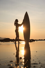 Silhouette of a surfer holding a surfboard at sunset, a woman enjoying the beach and sea, an active...