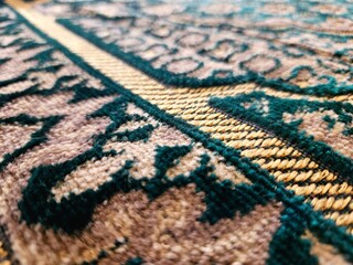 Fototapeta premium Macro shot of a decorative carpet, highlighting intricate patterns in green and beige with a bold golden border