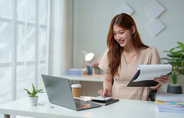 Asian businesswoman calculates company sales with a calculator Online financial information on...