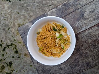 Delicious fried noodles or Mie Goreng with mixed vegetables in bowl on a wooden table.