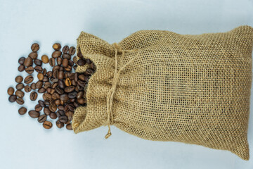 Burlap sack spilling roasted coffee beans on white background