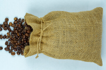 Burlap sack with roasted coffee beans spilling on white background