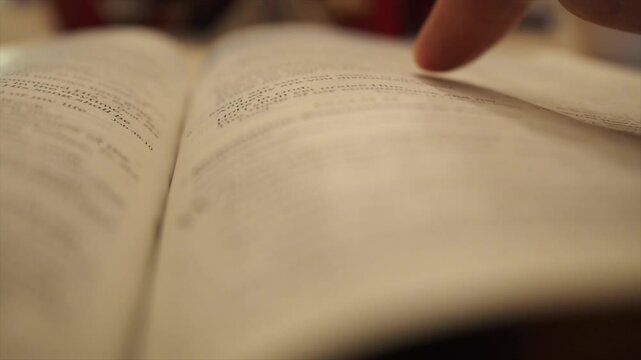 Closeup footage of a finger pointing at a paragraph on an open book, with blurred background