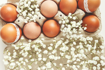 Brown Easter eggs decorated lace and white gypsophila flowers in carton on white background. Easter...