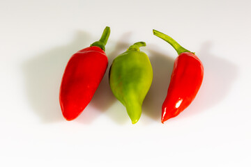 Three freshly harvested red and green chili peppers displayed o a white surface