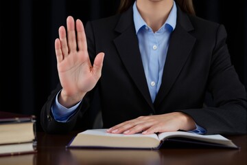 Businesswoman gesturing stop while seated at a desk with an open book in a professional setting.