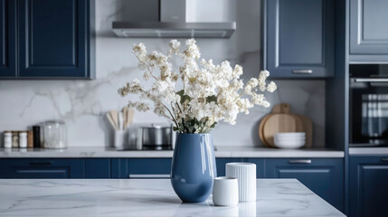 Kitchen in scandinavian style with island table, blue furniture and modern kitchenware. Bright interior with white walls and floor. Vase with flowers on marble countertop.