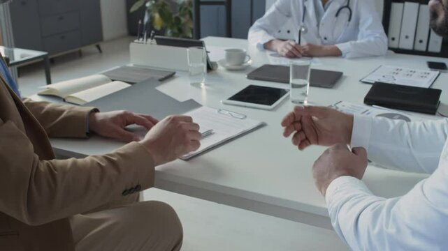 Close up view of unrecognizable male client signing agreement and shaking hands with medical professional during meeting in clinic