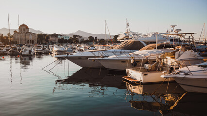 Close-up of a yacht's bow in a marina in Greece, surrounded by clear reflections of masts on the calm water