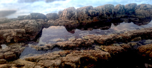 Tide pools reflecting cloudy sky and rocks on the seashore