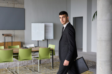 A determined businessman in a black suit confidently walks through the office, embodying professionalism and focus as he heads towards new challenges