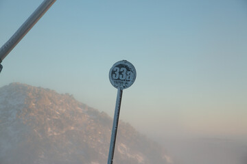 Close-up of a frosty ski slope marker "33a" against a misty mountain landscape during sunrise.