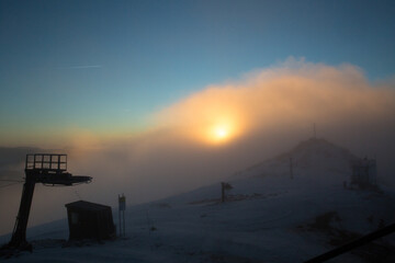 A breathtaking sunrise over a snowy mountain peak, partially covered by fog and mist.