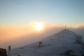 A breathtaking sunrise over a snowy mountain peak, partially covered by fog and mist.