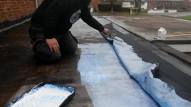Worker applying waterproof underlayment beneath a rubber roofing membrane on a flat roof. Showcasing roof sealing, insulation, and weatherproofing in residential construction.