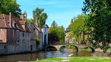 Naklejka premium A serene view of a canal in Brugge, Belgium. Colorful buildings line the water, and a charming bridge arches over. The still water mirrors the sky, making it an ideal relaxing getaway.