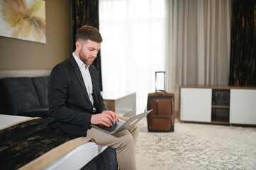 Young businessman working with computer sit on bed in hotel room