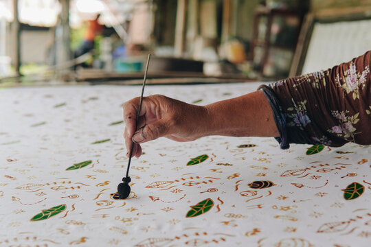 Close up picture of a person's hand drawing the design pattern of Indonesian batik tulis fabric.