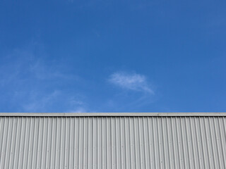 Fototapeta premium Industrial factory building with aluminum metal texture on the exterior wall against the background of blue sky and clouds, modern architecture of corrugated steel facade. Copyspace, design.