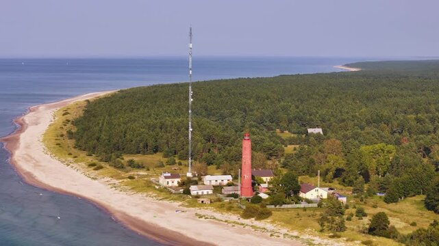 Aerial view of a bricked orange lighthouse construction in a wild forested beach landscape of Latvia