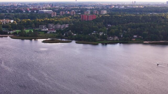 Aerial view of Ķī&scaron;ezers iake in Riga, Latvia, with primary inflow of the Jugla River, drone fly at sunset with cityscape at distance