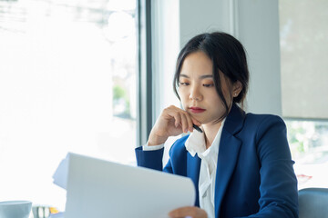 Businesswoman sitting at desk on couch in workplace or at home working on laptop and analyzing data on charts and graphs and writing on papers to make business plan and strategies for company, startup