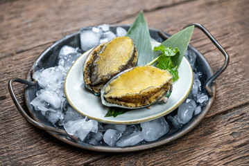 Fresh Sashimi Abalones in black plate with ice on wooden background, Fresh Abalones in black plate on wooden table.