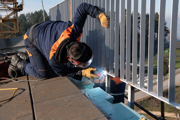Industrial welder skillfully crafts a metal fence for a new business complex, using modern...