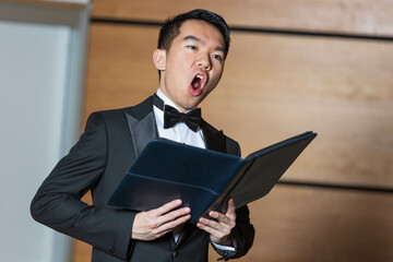 A man is wearing a tuxedo and singing joyfully into a microphone