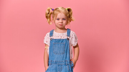 Cute, little girl shows tearful expression, looking at camera with bandage on arm, against pastel pink background. Concept of healthcare, protection, immunity, prevention.