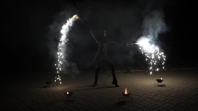 The artist of the fire show throws fire sparks into the air. It's an impressive and beautiful performance, with fire and fireworks, in slow motion. A professional circus performer dances with fire. 