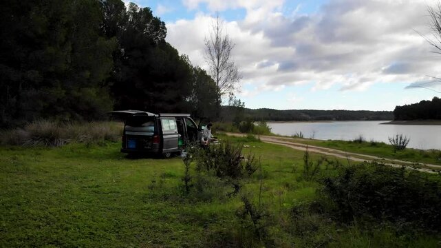 4K Drone footage of woman having breakfast at a Camper van in nature with stunning lake and forest view somewhere in Valencia, Spain. High quality 4k footage