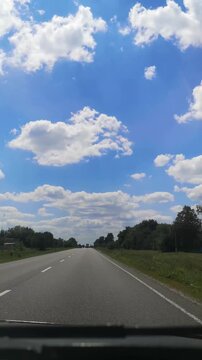 Front windshield view of a car driving on a paved road through summer tree lines under a picturesque cloudy sky. Vertical 4k video, 10 seconds. Truck approaches from the opposite direction