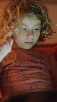 small girl plays or watches a tablet computer in vertical
