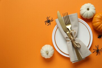 Halloween table with white plate, cultery, pumpkins, bats and spiders on color background