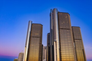 Fototapeta premium Iconic Detroit skyscrapers at twilight, showcasing modern architecture against a vibrant sky. Golden hour light reflects on the glass facades. GMRENCEN, DETROIT, MICHIGAN, UNITED STATES